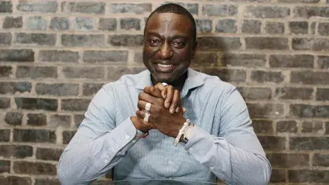 Yusef Salaam with hands clasped leaning against a brick wall