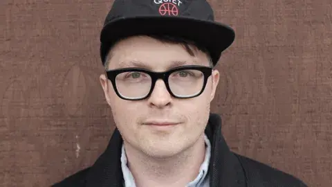 Matthew Dickman in a ball cap and glasses