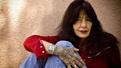 Joy Harjo wearing a red shirt and jeans showing her tattooed hand