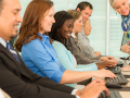 A woman is seen instructing a row of adults seated at computers