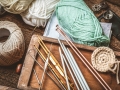 Yarn, knitting needles, and crochet hooks spread across a wooden table.
