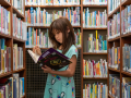 Standing girl, reading a book, surrounded by bookshelves