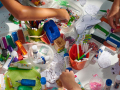 A table covered in colorful and glittery arts and crafts supplies, with various young people's hands shown reaching into the containers.