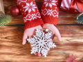 Child’s hands in a red and white sweater holding a wooden snowflake ornament.