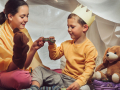 Two children engage in a tea party inside of a blanket fort