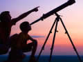 Child and adult pointing up at the night sky with a telescope