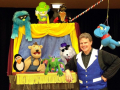 A puppet show performer poses with his puppets and puppet theater
