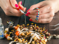 A pair of hands makes a piece of jewelry with pliers and assorted beads.
