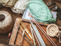 Yarn, knitting needles, and crochet hooks spread across a wooden table.