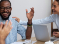 Group of Adults sitting a table with an open laptop discussing business topics