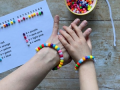 cup of beads, paper template describing which bead goes with which number, two hands wearing colorful beaded bracelets.