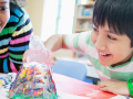 A smiling boy and girl lean over a table with a bubbling volcano experiment on it.