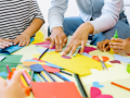 Children and an adult gather around colorful art supplies scattered on a table. 