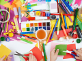 An assortment of craft supplies, paints, markers and hands with scissors cutting paper.