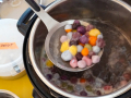 A ladle full of colorful dumplings over a large pot of dumplings.