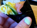 A hand holding a cone shaped roll of seaweed filled with rice and fresh fillings
