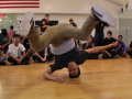 A man is demonstrating a breakdance move with participants watching from the side