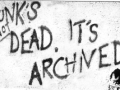 Black spray paint on a white wall "punks not dead. It's archived."  