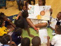 Woman holding an oversized picture book reading to a group of children.