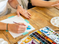 Person using a paintbrush and colored paint to create a watercolor illustration ona table. 