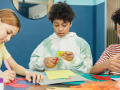 Three children cutting pieces of colorful construction paper. 