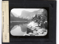 A black and white slide from the California Camera Club, a group of men and women are gathered on the shore of a lake, they are wearing clothing typical of the early 1900s