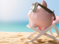 A relaxing, pink piggy bank wearing sunglasses sitting on a beach chair at the beach