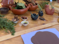 A table with flat clay, pots and cups made out of clay and other leafy greens.