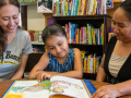 A literacy instructor, a young girl and a woman sit at a table and read a picture book.