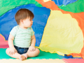 Baby sits on a colorful floor in front of an equally colorful parachute.