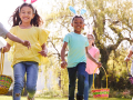 Group of children wearing bunny ears running to pick up Easter eggs during Easter egg hunt.