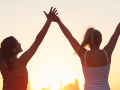 Two women exercising outside with arms raised.