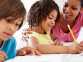 Adult assisting a child with written homework while another student works nearby
