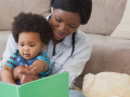 A woman holds a toddler in her lap while they read a book together