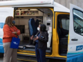 two people talking in front of a blue and white medical van