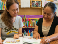 Literacy tutor and adult learner sitting at a table reading a book together