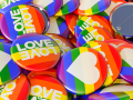 Many brightly colored pins featuring rainbow backgrounds, hearts, and the words "love is love"