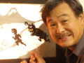 Sunny Seki holds shadow puppets against a projected screen.