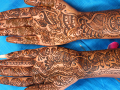 Hands and forearms decorated with detailed henna designs resting on blue fabric background.