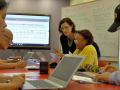 Instructor in a classroom with a diverse group of students using laptops.