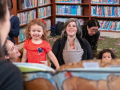 Babies and toddlers with grownups look to a person holding a book