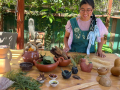 A woman sitting down with clay sculptures and plants surrounding her.