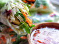 Fresh vegetable spring rolls filled with cabbage, carrots, and greens on a plate, served with a bowl of sweet chili sauce, creating a vibrant, appetizing scene.
